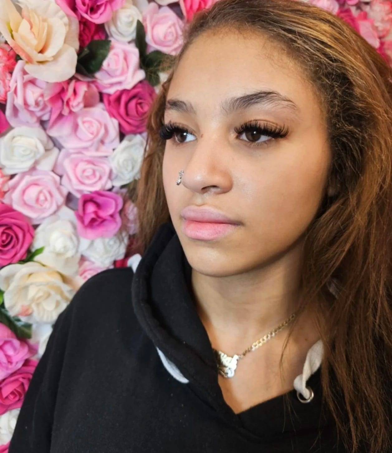 Defined lash set with shaped brows in front of a rose flower wall